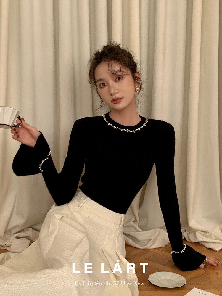 Woman wearing a black long-sleeve top with pearl trim and cream wide-leg pants.