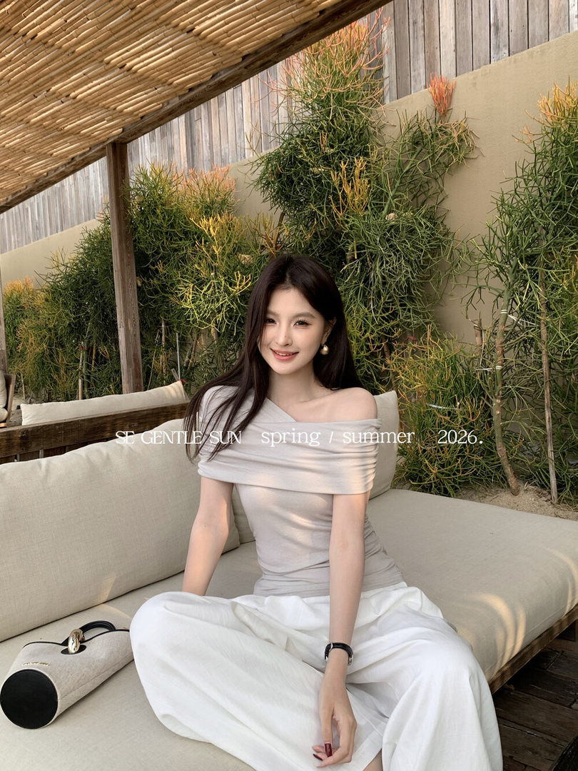 Woman wearing a light off-shoulder top and white pants on an outdoor lounge sofa