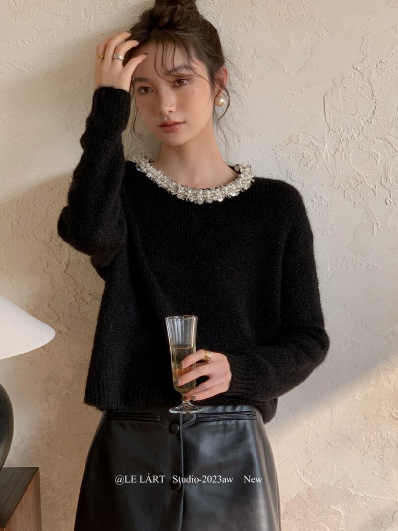 Model wearing a black fuzzy sweater with an embellished neckline and a black leather skirt