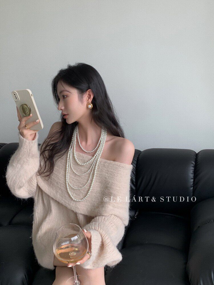 Woman wearing a beige off-shoulder fuzzy knit sweater with layered pearl necklaces