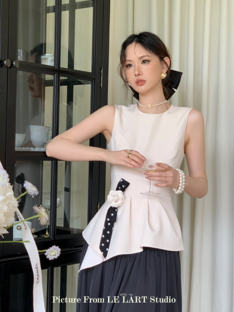 Woman wearing a sleeveless cream peplum top with a dark pleated skirt