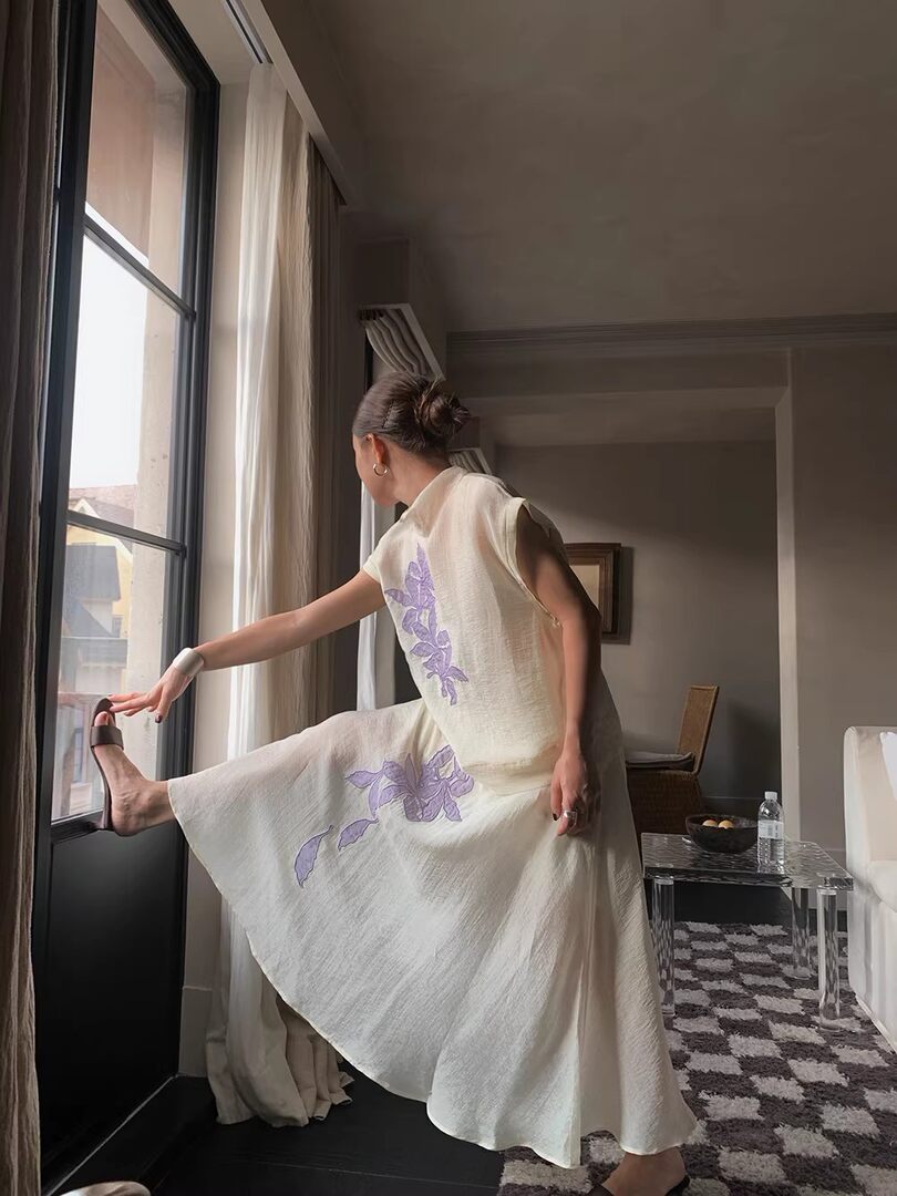 Woman wearing a sleeveless cream floral midi dress by a window