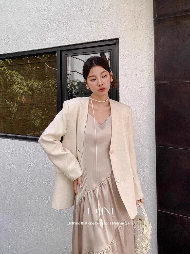 Model wearing a cream blazer over a satin dress, holding a small handbag