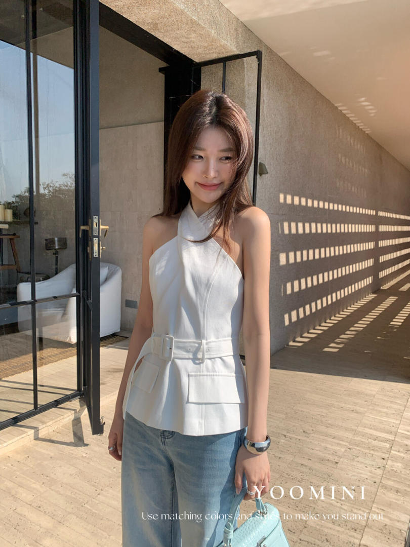 Woman wearing a white halter top with a belt detail and light blue jeans