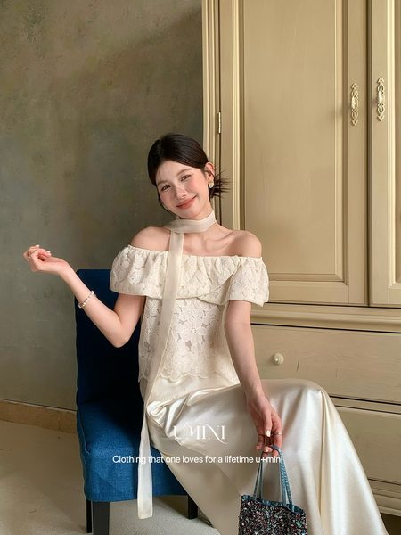Model wearing an off-the-shoulder cream lace dress with a long scarf tie