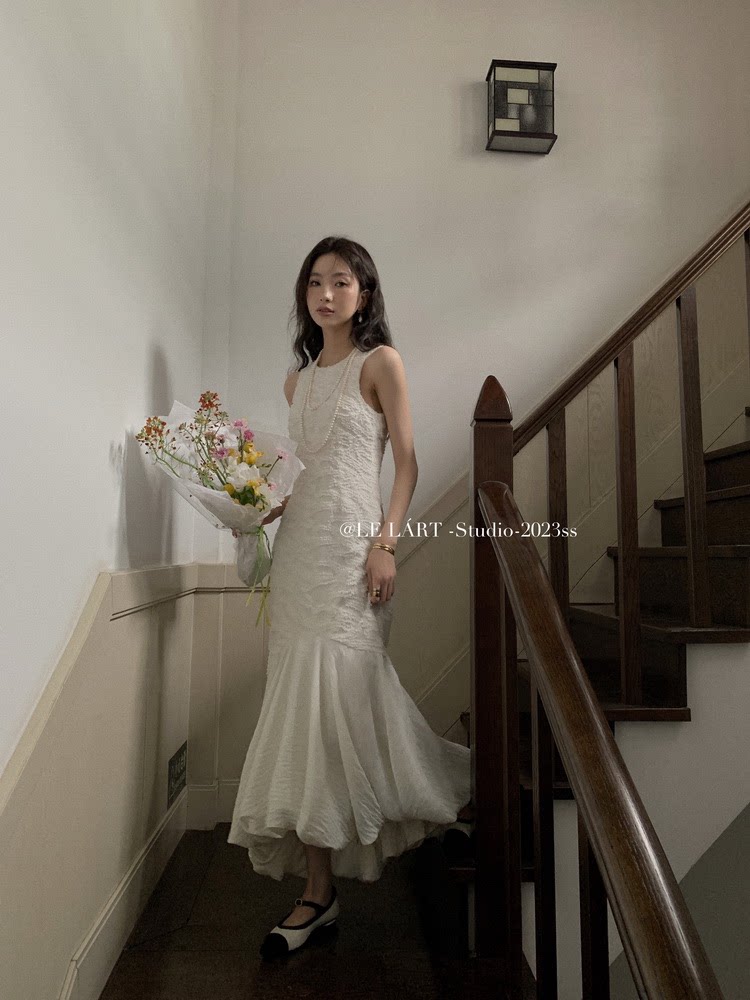 White sleeveless mermaid-style dress worn by a model on a staircase