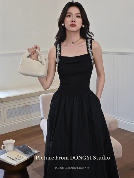 Black sleeveless dress worn by a model holding a beige handbag
