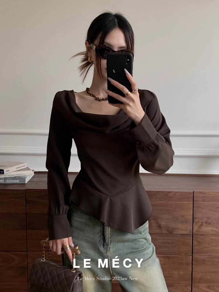 Woman wearing a dark brown long-sleeve draped top and jeans, holding a quilted handbag