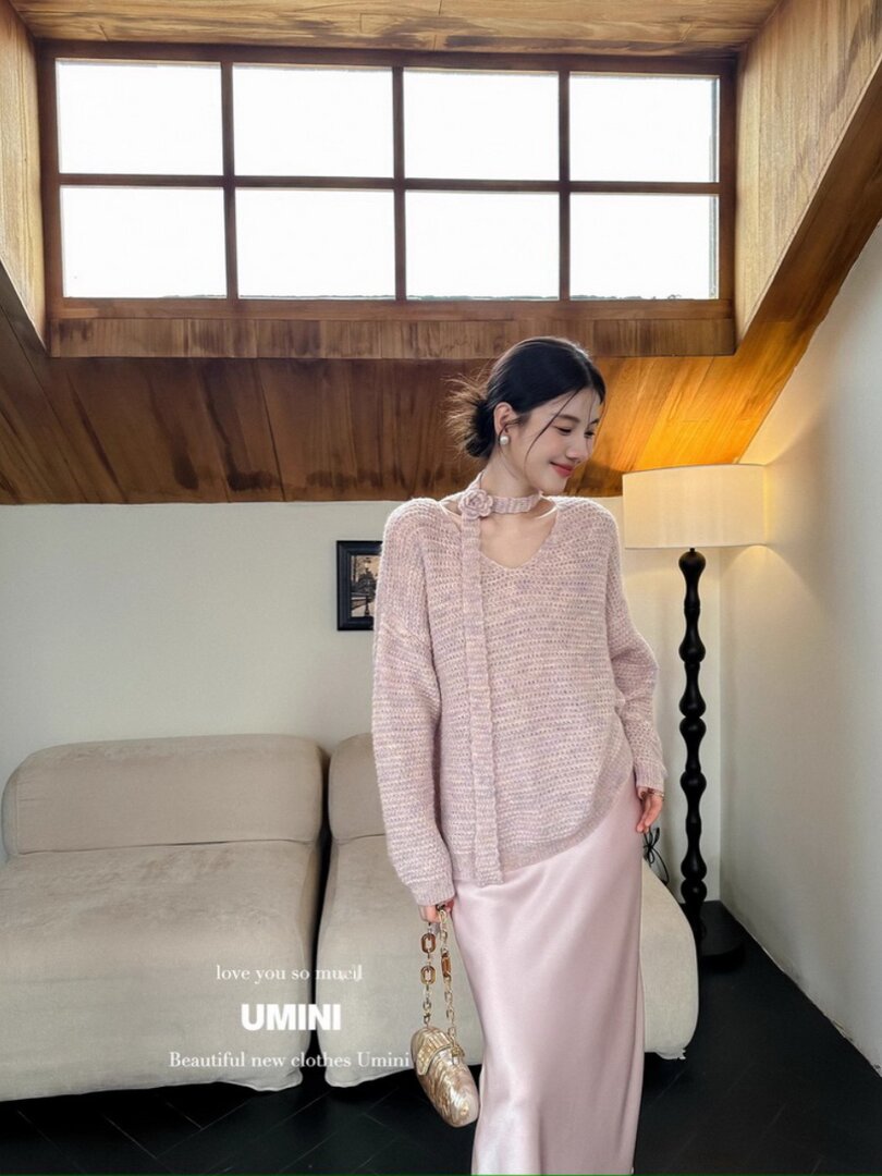 Woman wearing a light pink knit sweater and satin skirt in a room setting