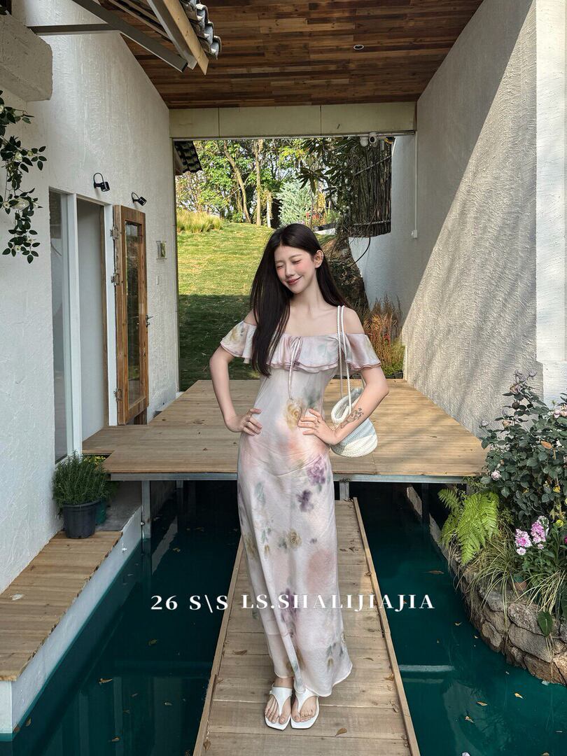 Woman wearing a pastel floral off-shoulder maxi dress with white sandals and a woven bag.