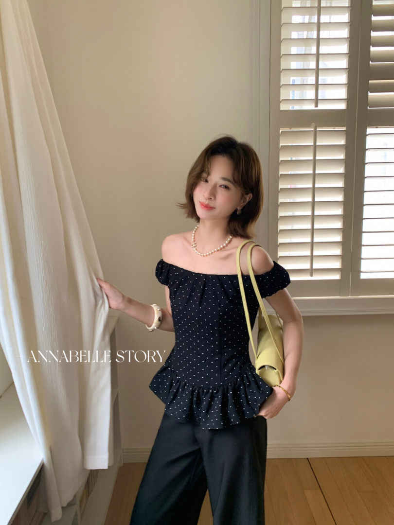 Model wearing a black off-shoulder polka dot ruffle top with black pants
