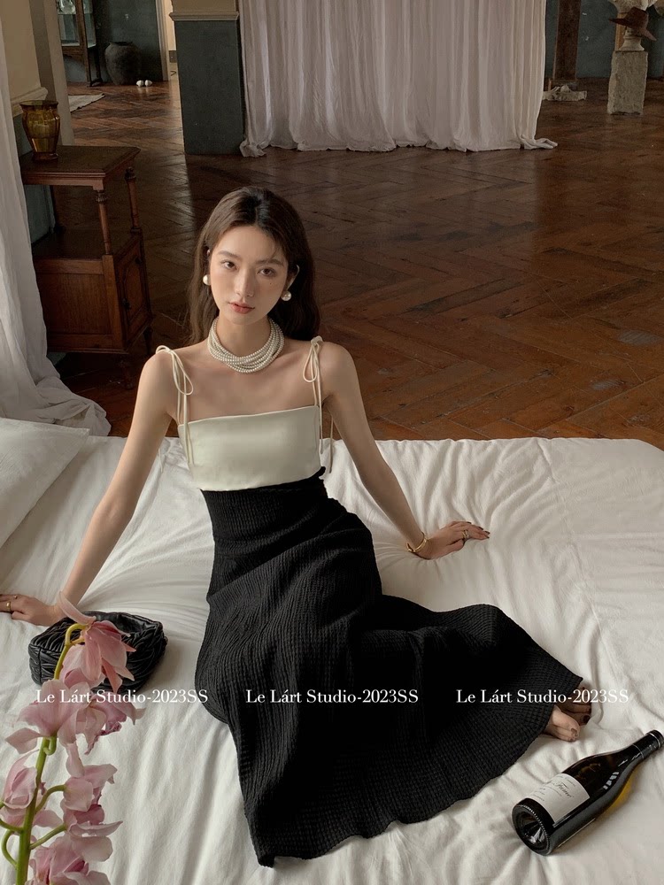 Model wearing a black and cream sleeveless maxi dress on a bed