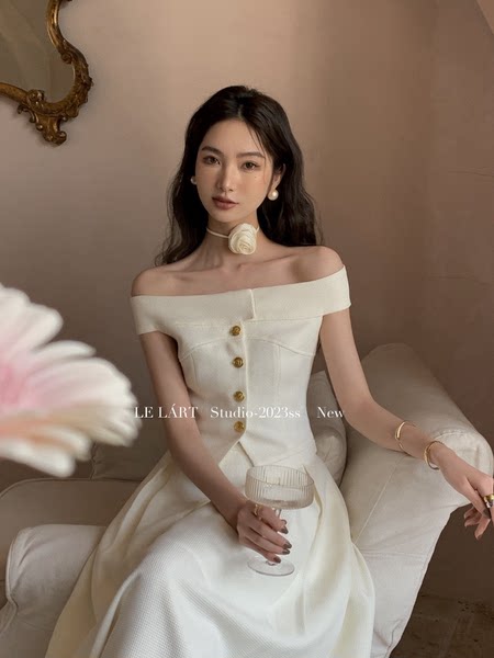 Woman wearing an off-shoulder white dress with gold buttons