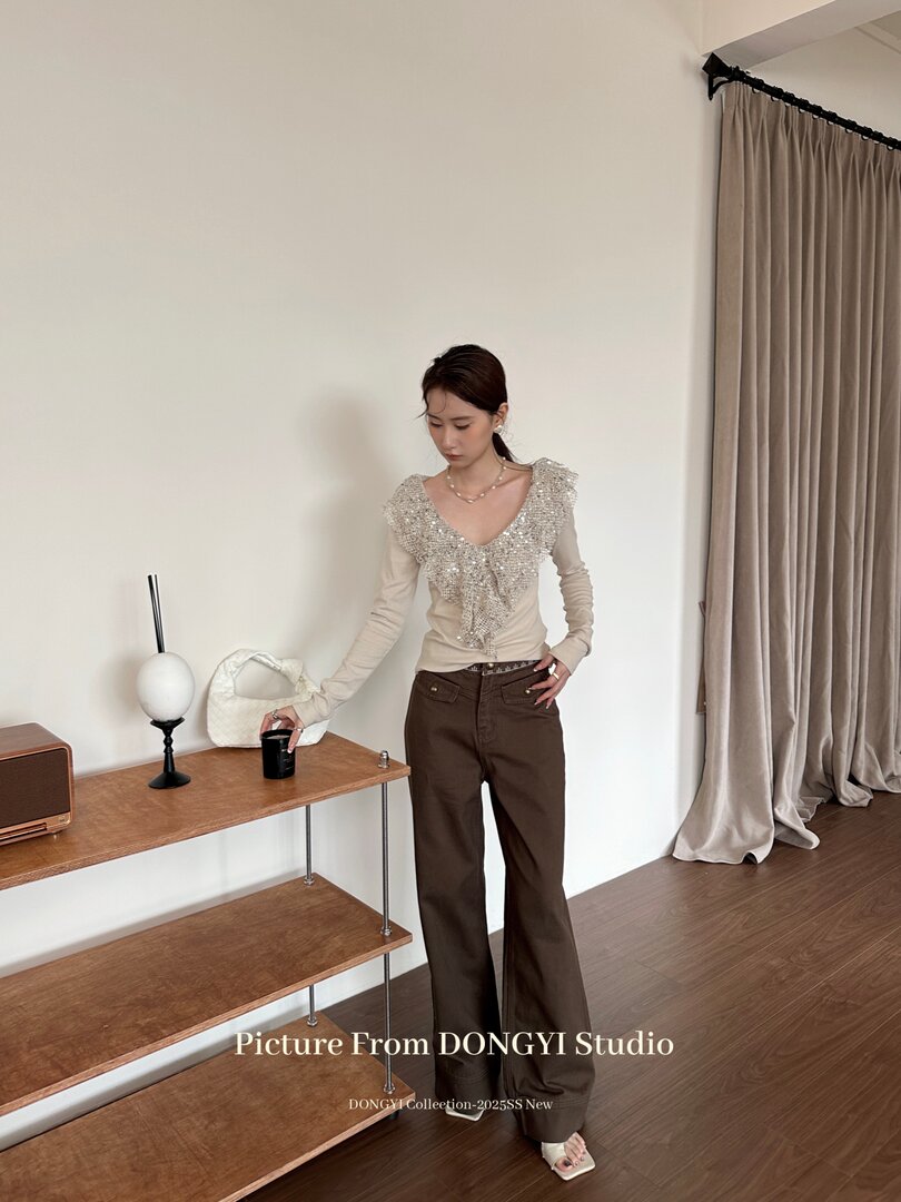 Model wearing a beige embellished long-sleeve top with brown wide-leg pants
