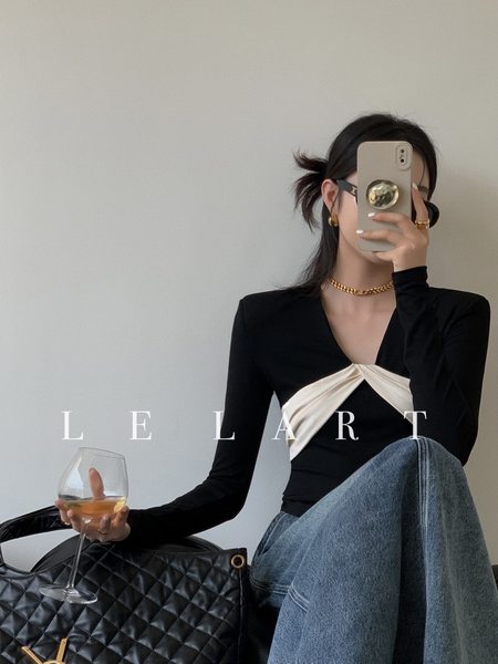 Woman wearing a black long-sleeve wrap top with cream detail and blue jeans, holding a quilted black handbag
