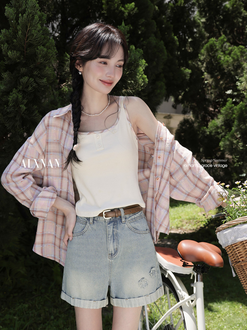 Woman wearing a plaid shirt over a tank top with denim shorts outdoors