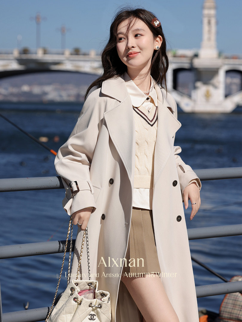 Woman wearing a beige trench coat and cream knit outfit by the waterfront