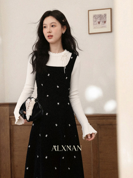 Model wearing a black pinafore dress with a white ribbed blouse and small star pattern