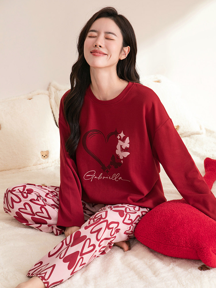 Red heart-print loungewear pajamas worn by a woman sitting on a bed