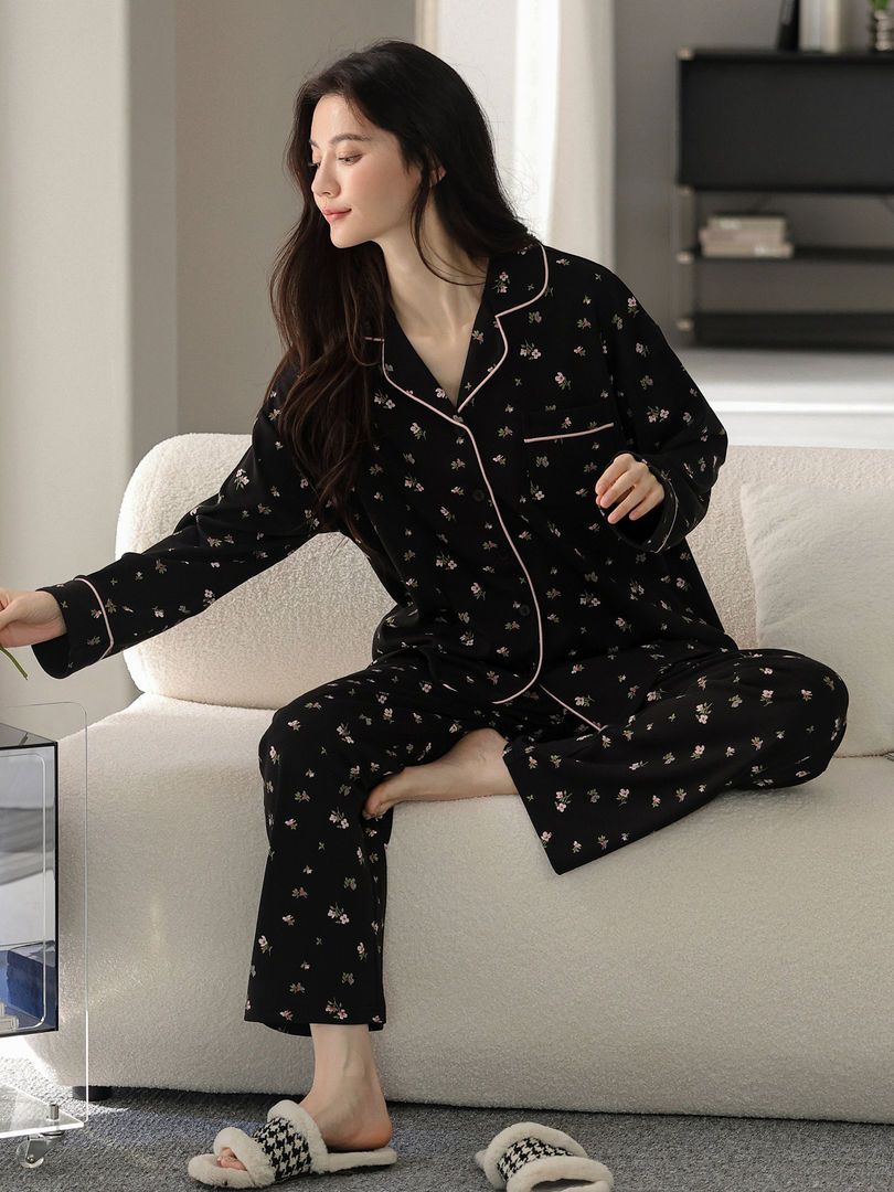 Woman wearing black floral pajama set with pink piping on a sofa