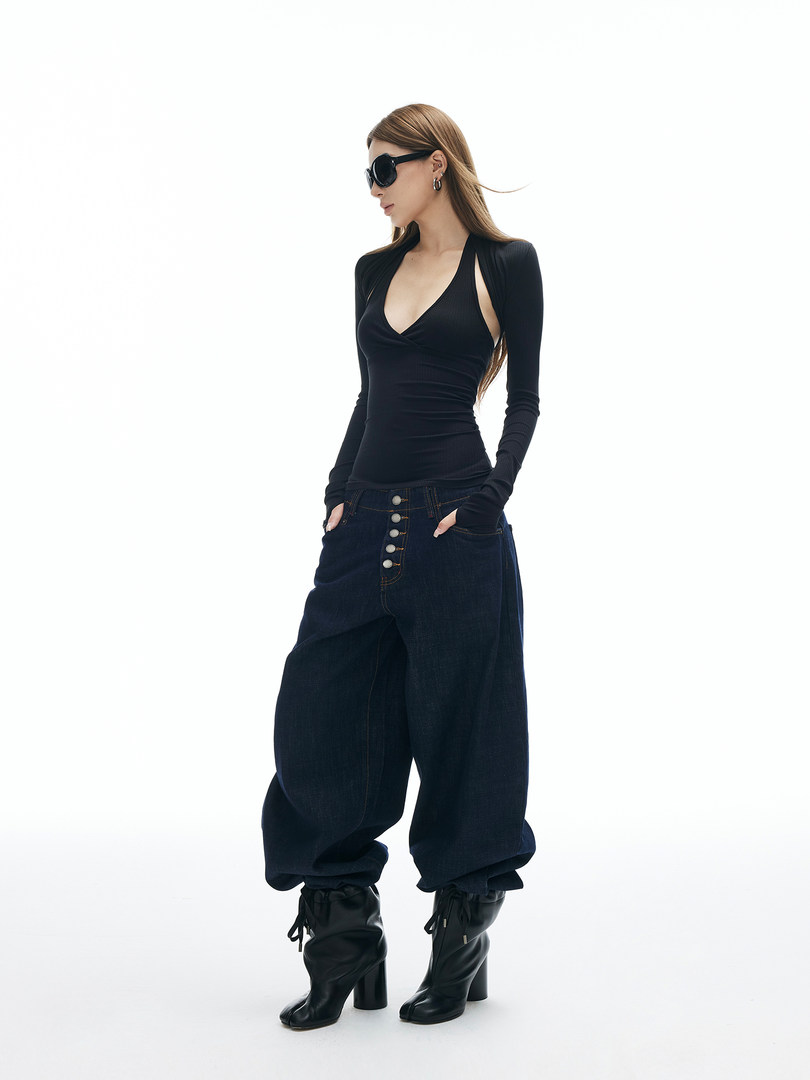 Fashion model wearing a black long-sleeve top, wide-leg jeans, and black boots on a white background