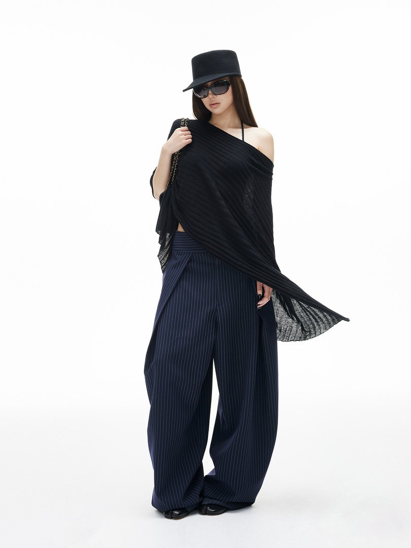 Fashion model wearing a black draped top, pinstripe wide-leg pants, hat, and sunglasses