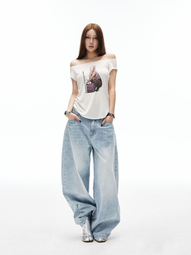 Model wearing a white off-shoulder graphic tee and baggy light-wash jeans