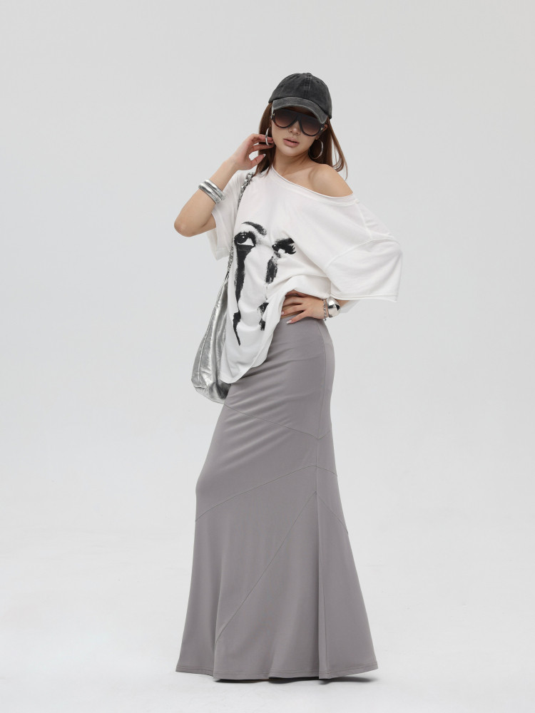 Model wearing a white graphic off-shoulder top with a long gray skirt and accessories