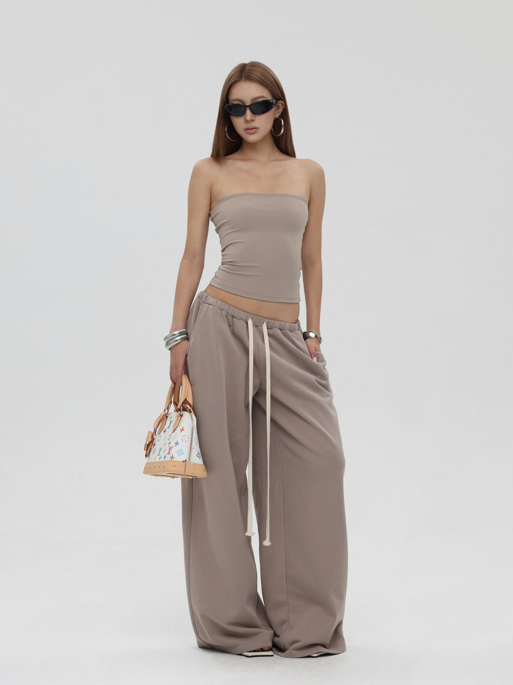 Model wearing a beige strapless tube top with wide-leg drawstring pants and a small handbag