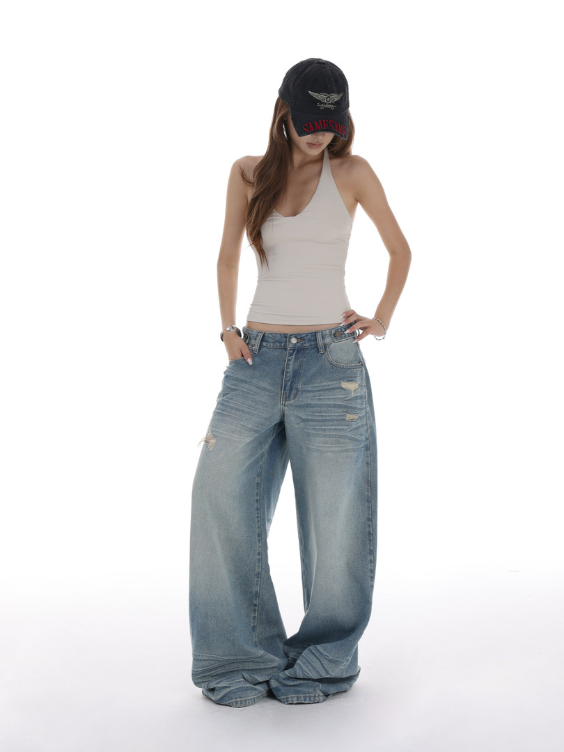 Model wearing distressed wide-leg jeans with a white halter top and black cap