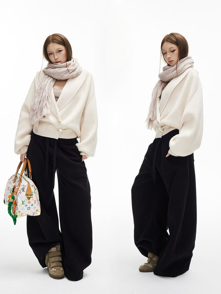 Model wearing a cream wrap sweater with scarf, black wide-leg pants, and a patterned handbag