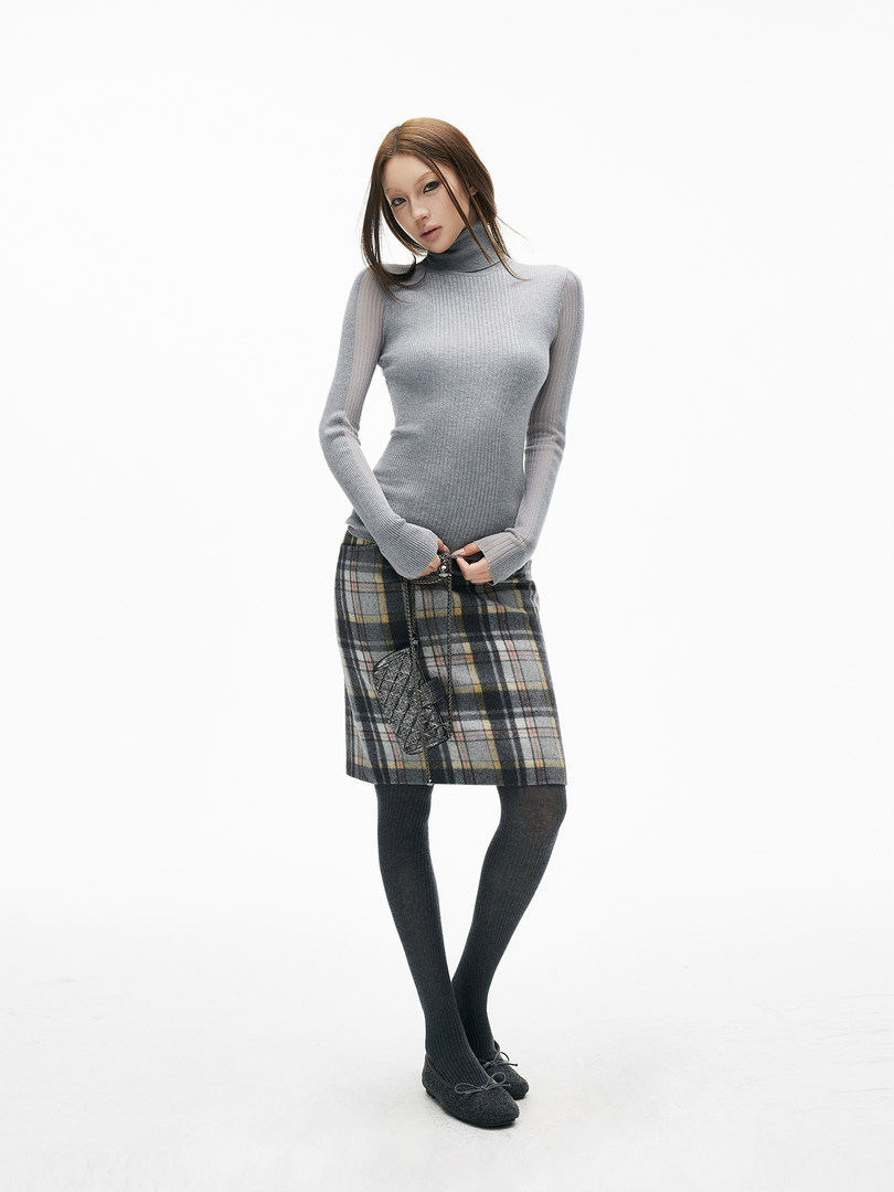Woman wearing a gray turtleneck sweater with a plaid skirt, tights, and flats