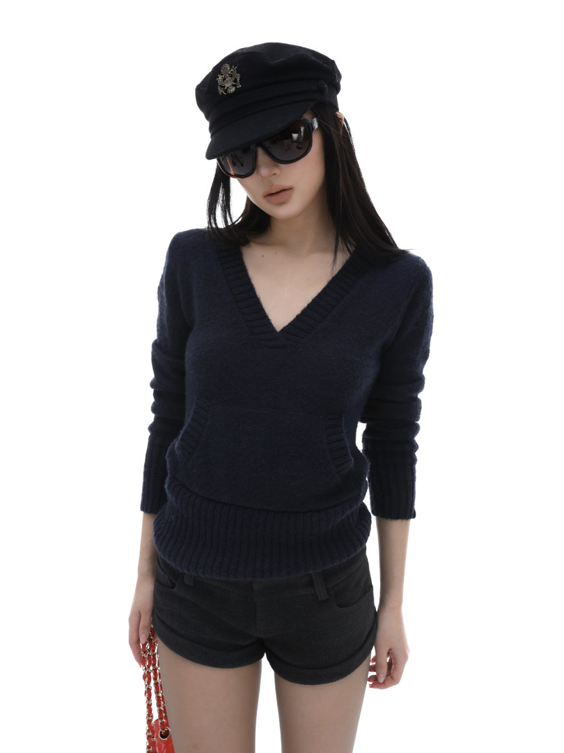 Model wearing a black knit V-neck top with black shorts, cap, and sunglasses