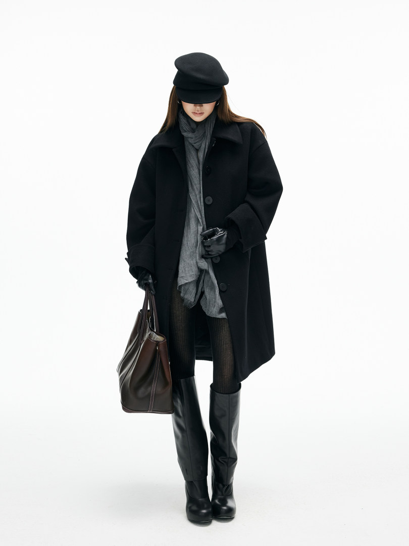 Fashion model wearing a black coat, hat, gloves, boots, and carrying a leather tote bag