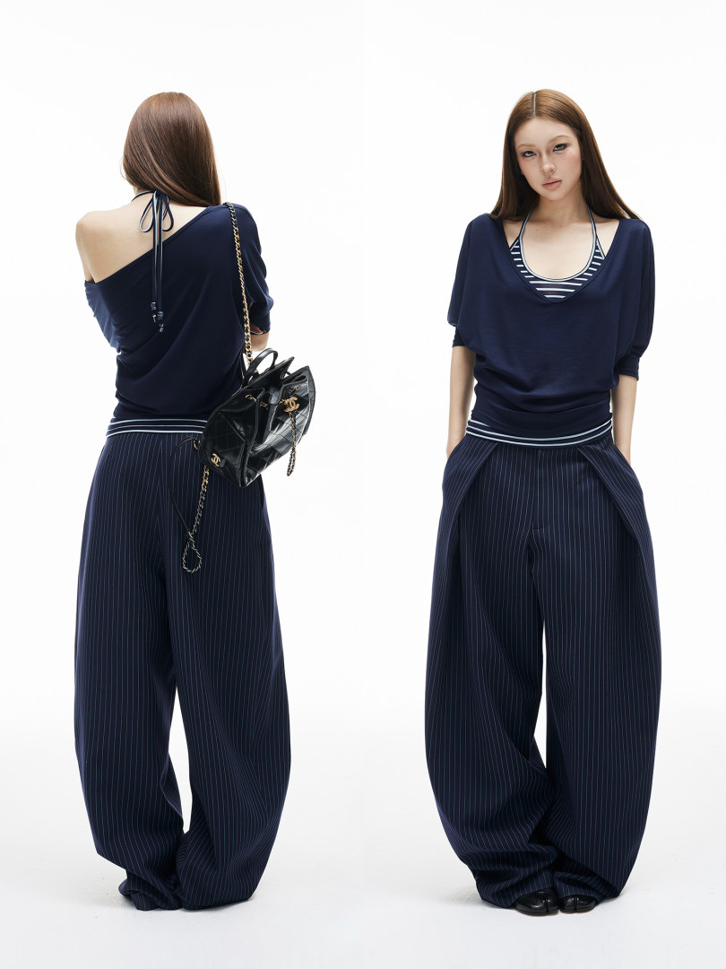 Model wearing a navy draped top and wide-leg pinstripe pants with a chain handbag