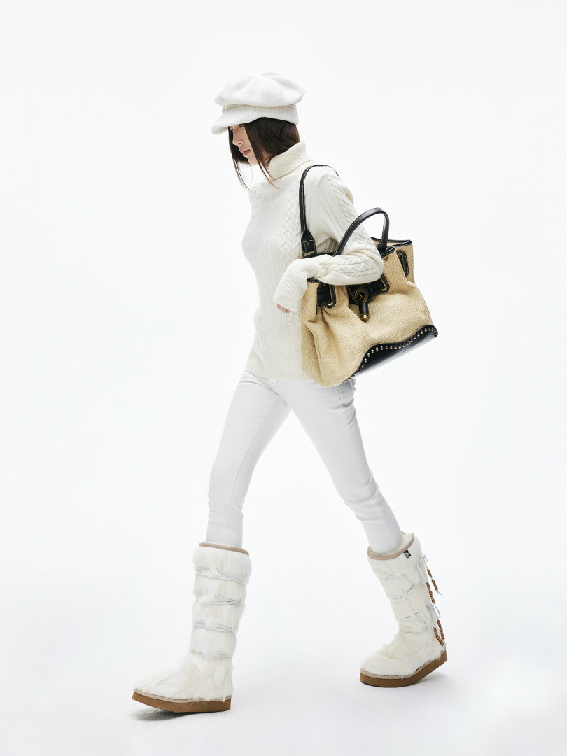 Woman modeling a white winter outfit with fur boots and a tan handbag