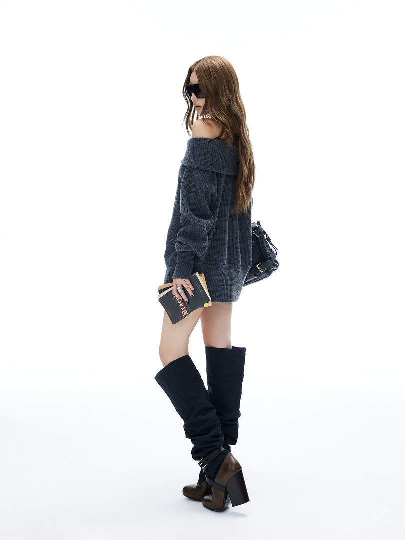 Model wearing a dark off-shoulder knit sweater dress with tall heeled boots and a small handbag