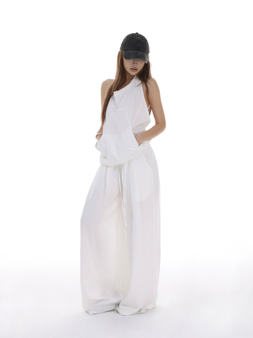 Model wearing a white wide-leg outfit with a black cap on a white background