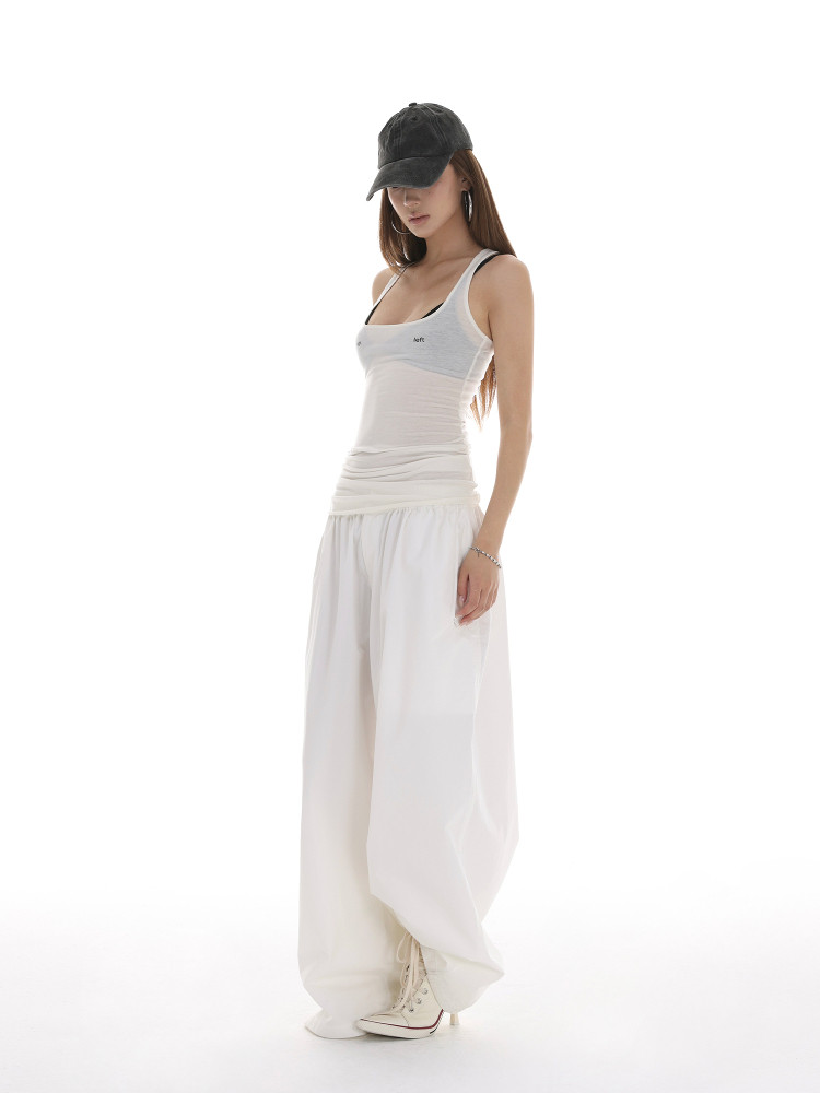 Model wearing a white tank top and loose white pants with a black cap