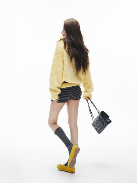 Model wearing a pale yellow fuzzy sweater with striped shorts, socks, yellow flats, and a black quilted handbag