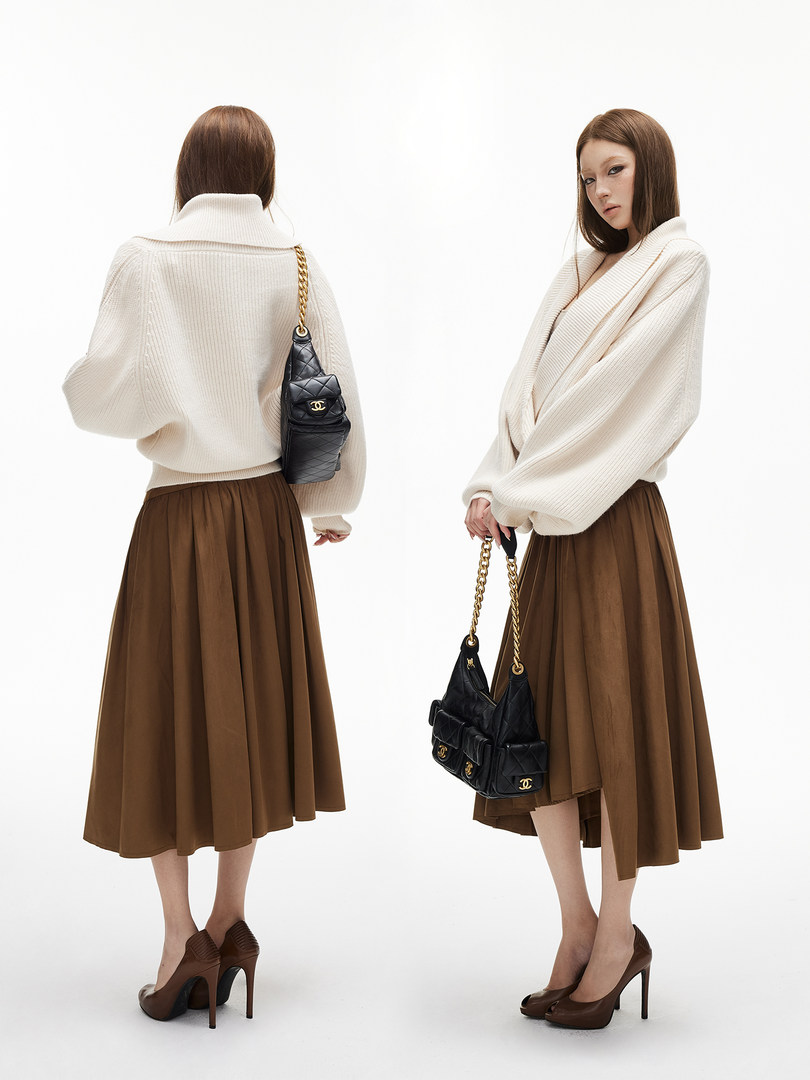 Model wearing a cream oversized sweater with a brown midi skirt, black quilted handbag, and brown heels