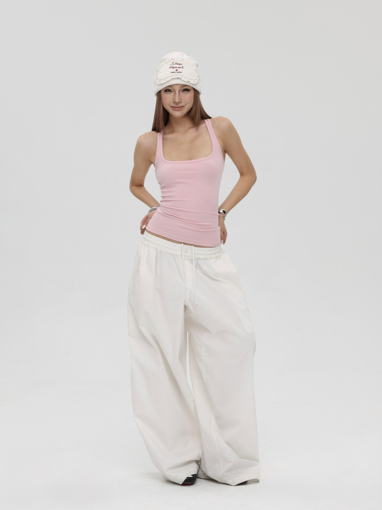 Model wearing a pink tank top, white wide-leg pants, and a white hat