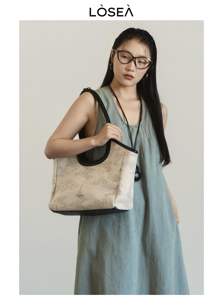Model wearing a light blue sleeveless dress and carrying a beige tote bag