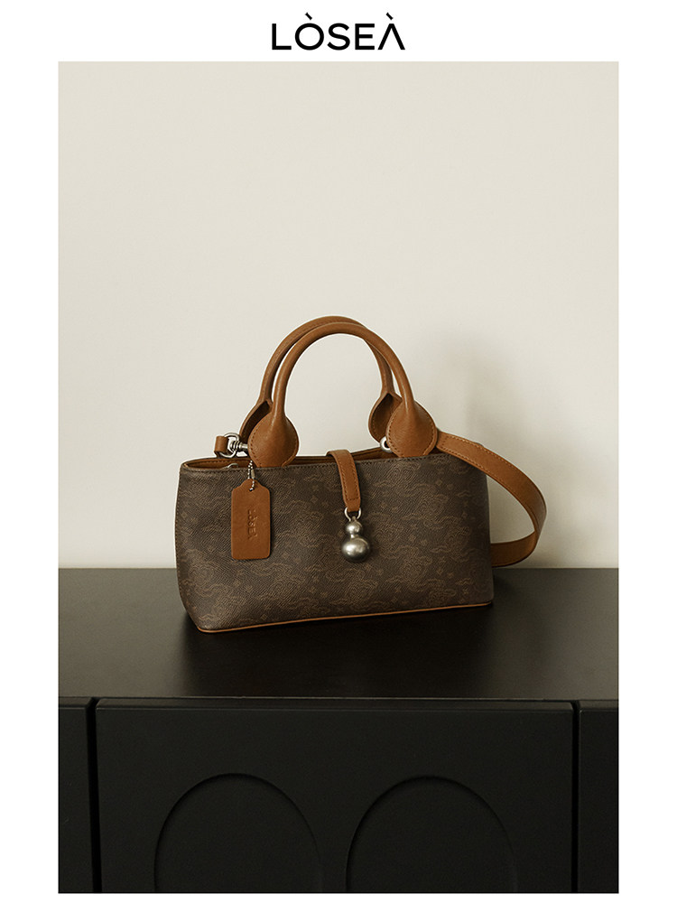 Brown leather handbag with shoulder strap on a black surface