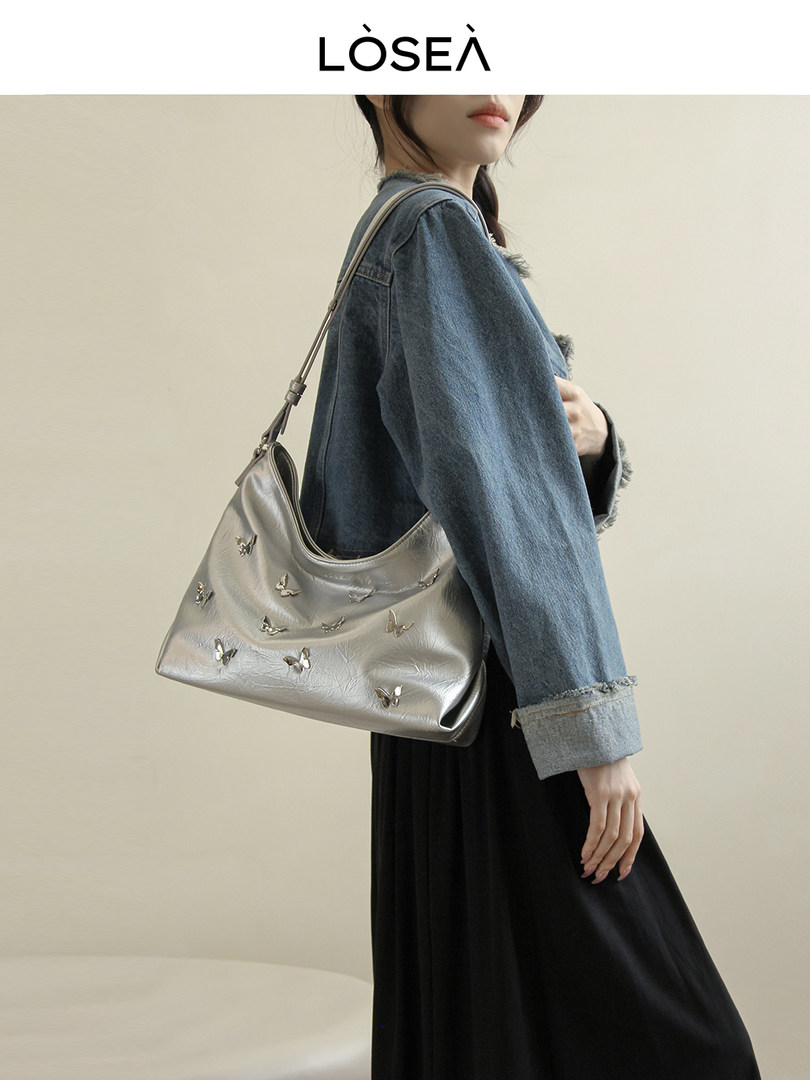 Silver shoulder handbag with butterfly details worn by a model