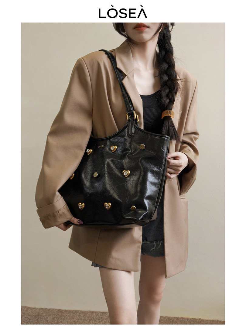 Model wearing a black leather tote bag with gold stud details