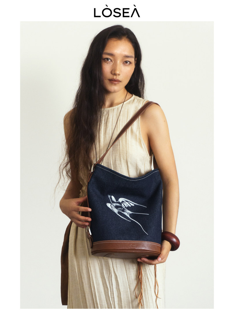 Model wearing a navy crossbody shoulder bag with brown leather trim