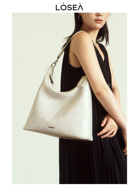 Beige shoulder handbag worn by a model in a black dress