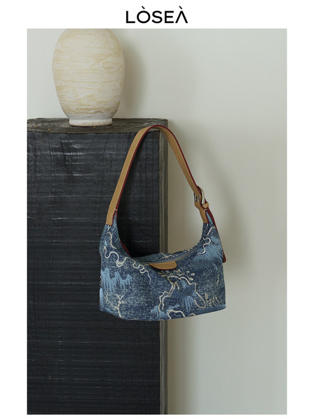 Blue denim shoulder bag with tan strap on display