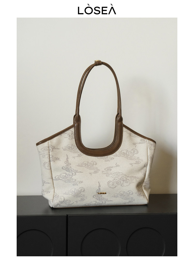 Beige patterned tote handbag with brown handles on a display surface